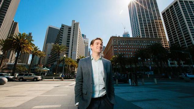 Student walks down the street with SF skyline behind him.