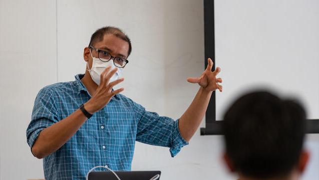 Professor gesturing with both hands lectures at a podium