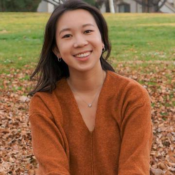 Student sits on a pile of leaves and smiles.