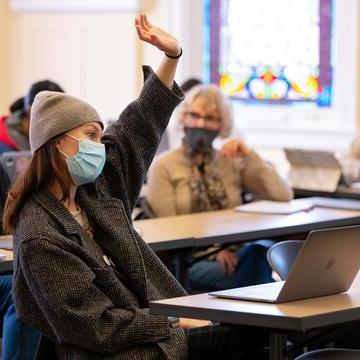 Student sitting at a table raises hand in class